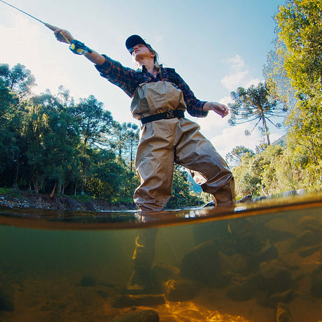 Low angle view of a woman casting a fly rod while wading in a river